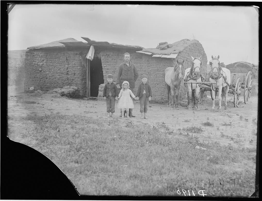 George Barnes and family pose in front of their caved-in sod house in 1887. The Nebraska homesteader’s wife had died the year before. Early Nebraska photographer Solomon Butcher titled his photo, “Three motherless children and a caved in soddy.”