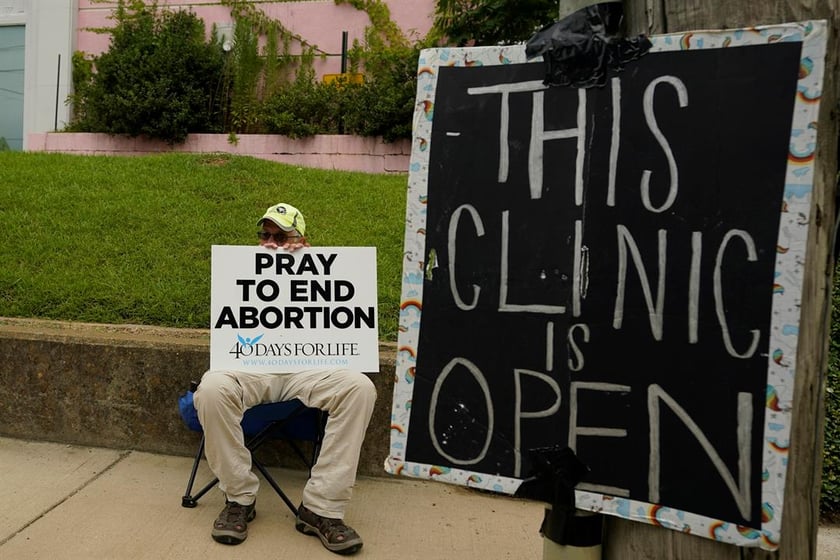 An anti-abortion supporter sits behind a sign that advises the Jackson Women's Health Organization clinic is still open in Jackson, Miss., July 6, 2022. (AP Photo/Rogelio V. Solis, File)